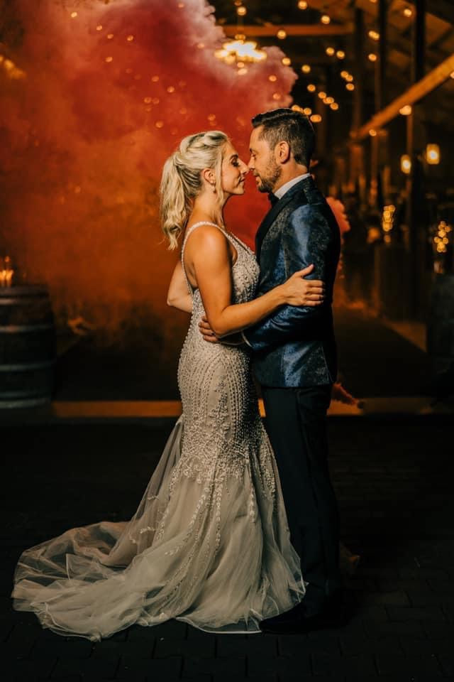 A couple embracing while colored smoke bombs go off in the background at an outside wedding venue in Knoxville